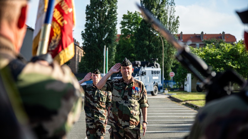 Le Général Christophe Daniel en treillis kaki au garde à vous. Au premier plan, dos, la garde au drapeau du GBGM.
