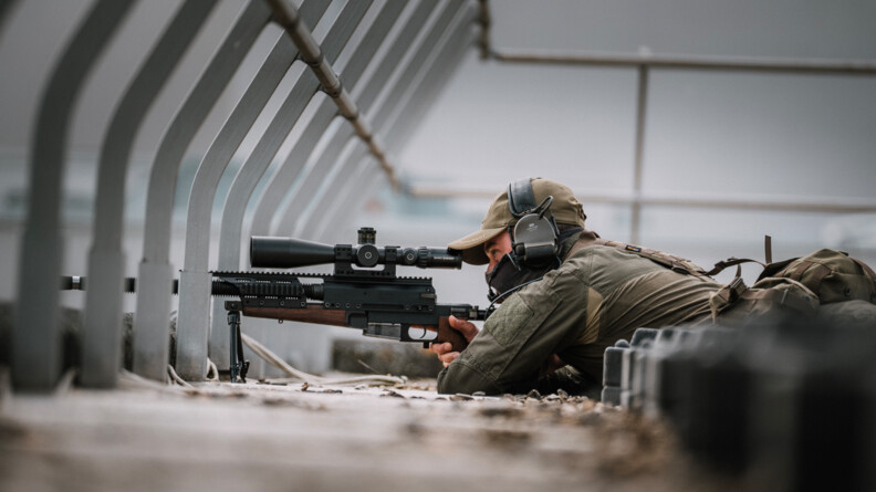 Agrandir l'image Un tireur d'élite gendarmerie en treillis de prolfil, allongé, le bras gauche replié et la main droite sur le fusil, autour,des structures grises bétonnées et métalisées