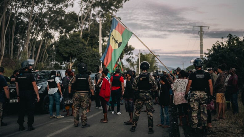 Des gendarmes en treillis, gilet pare balles et casque, en ligne en travers de la chaussée, face à une foule de manifestants.