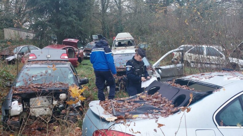 Deux gendarmes relevant les éléments au milieu d'un champ de véhicules épaves