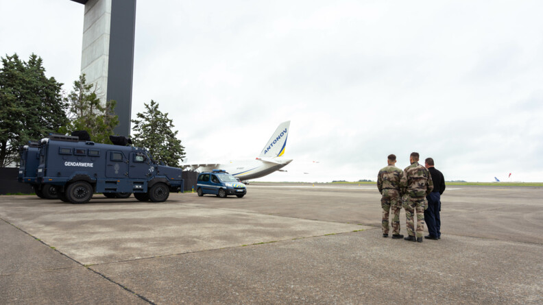 Agrandir l'image Un centaure, un partner gendarmrie, proche de l'arrière d'un Antonov sur le tarmac. A droite, trois gendarmes de dos regardent la scène