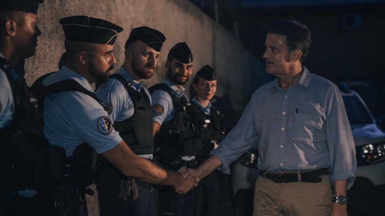 Le ministre des Outre-mer salue un gendarme. Il fait nuit.