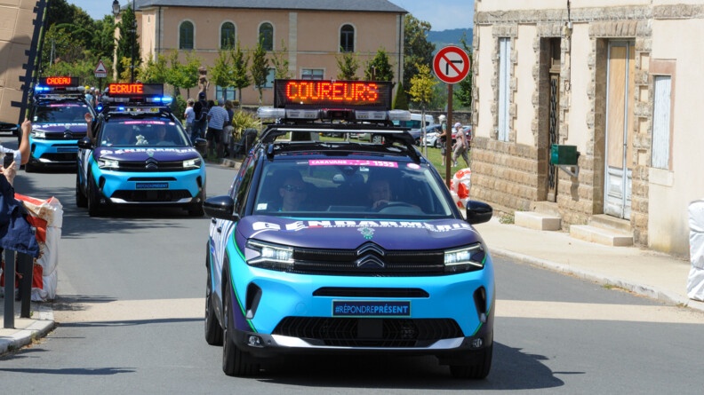 Agrandir l'image Trois véhicules de la caravane du Tour de France féminin roulent dans un village