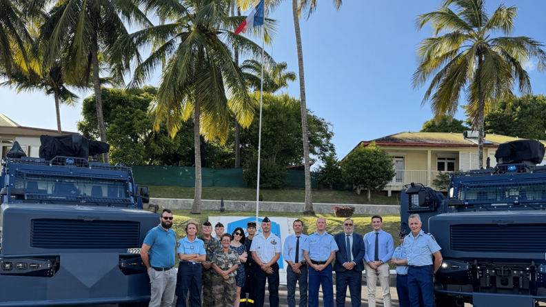 14 personnes civiles et militaires avec de part et d'autre des Centaure de la gendarmerie devant de la végétation et une maison à droite