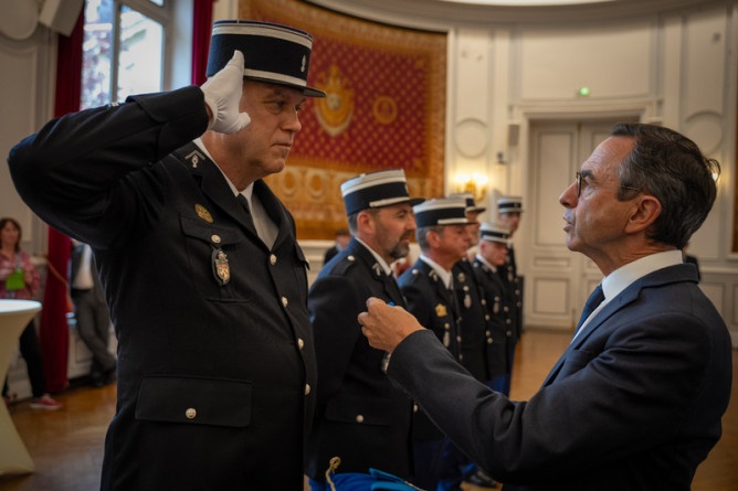 Agrandir l'image Le ministre de l'Intérieur, Bruno Retailleau, s'apprête à décorer un gendarme de la médaille du Mérite. Ce dernier effectue un salut militaire.