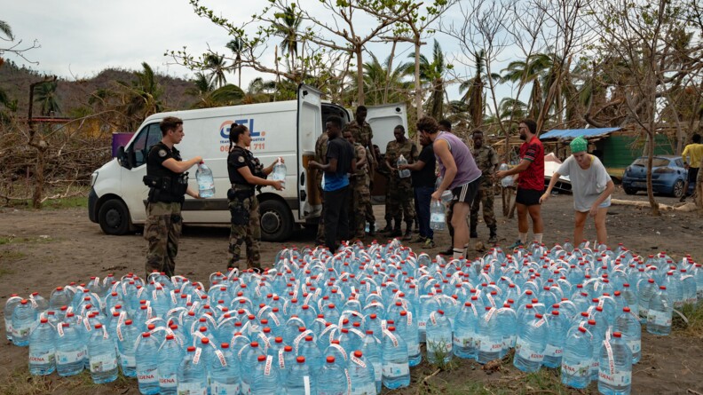 Des gendarmes en treillis et haut noir distribuent de l'eau &agrave; des civils, de nombreux bidons d'eau sont au sol