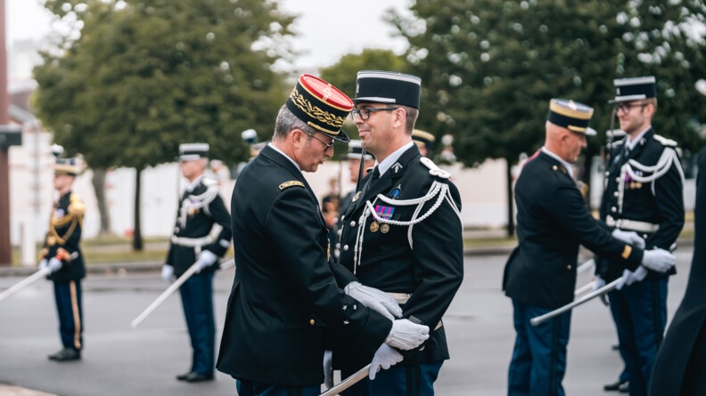 Agrandir l'image Un général de gendarmerie dévoile les galons de manche d'un gendarme. Le reste de la scène est floue mais à droite un colonel y effectue le même geste pour un autre gendarme