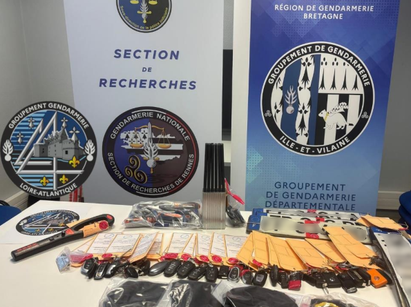 Sur une table, de nombreuses clés de voiture sous scellés, des plaques d'immatriculation,  et divers objets sous scellés, sur une table. Derrière la table, deux kakemonos de la Section de recherches de Rennes, du groupement de gendarmerie départementale (GGD) d'Ille-et-Vilaine, ainsi que la rondache du GGD d'Ille-et-Vilaine