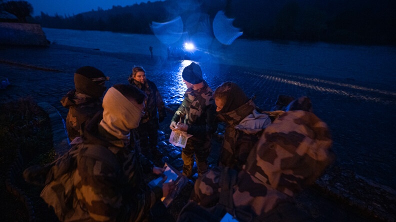 Au premier plan, des miliciens sont en cercles, en train de discuter. En arrière-plan, un quai où est amarré le zodiac de la gendarmerie des voies navigables avec des officiers-élèves autour.