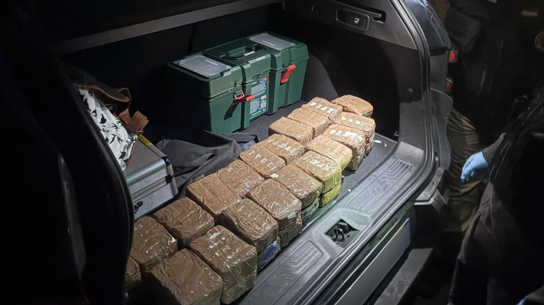 Agrandir l'image des pavés entourés de scotch marron dans un coffre de voiture. Une caisse verte type caisse à outil