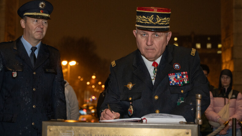 Un g&eacute;n&eacute;ral de gedarmerie regarde droit devant lui, en train de signer un registre, de nuit, en ville, sous la pluie. A gauche, un policier allemand