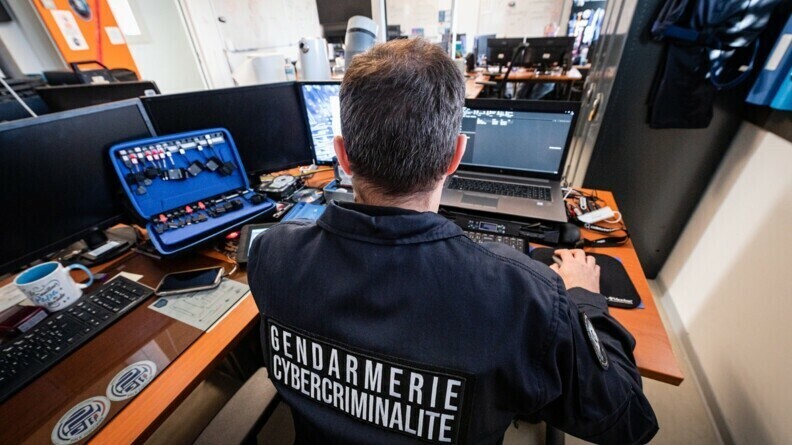un gendarme de dos devant des ordinateurs et matériel