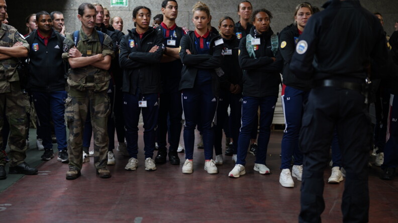 Face à un gendarme du GIGN, de dos et à droite de l'image, une quinzaine de sportifs de la Défense alignés. A gauche, deux militaires en treillis les accompagnent
