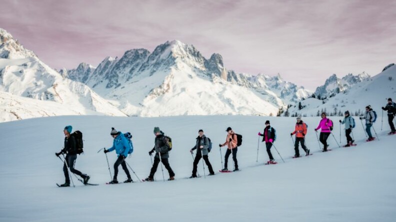Agrandir l'image File de randonneurs en raquettes sur la neige avec les sommets enneigés en arrière plan.