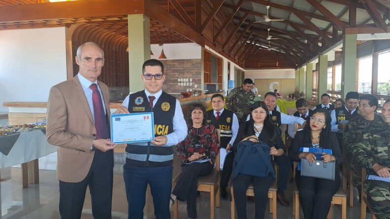Agrandir l'image L'officier de gendarmerie, en civil, remet son diplôme de formation à l'un des policiers péruviens, devant le reste des participants assis dans la salle.