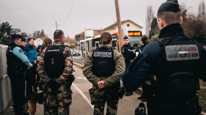 Agrandir l'image Des gendarmes français et des policiers suisses se tiennent debout, de dos ou de profil par rapport à l'objectif, sur un trottoir, alors qu'un autobus arrive à leur niveau