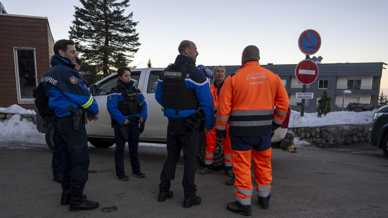 Quatre gendarmes discutent avec deux personnels de la commune en tenue orange, devant un pick-up blanc et des bâtiment gris et blancs modernes
