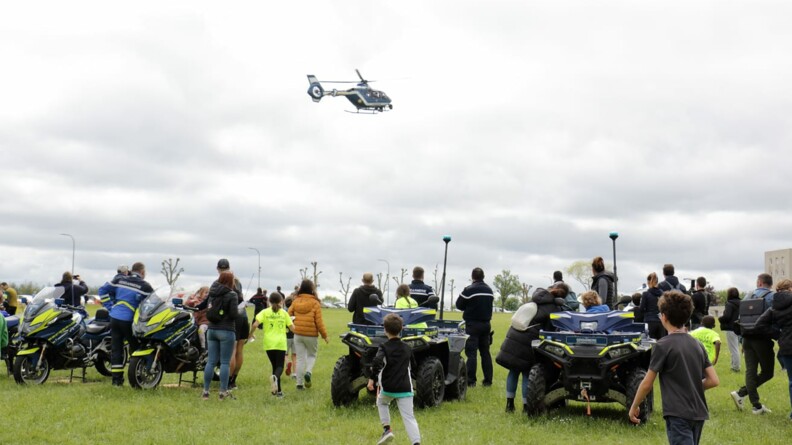 Agrandir l'image Des gendarmes et familles regardent un hélicoptère gendarmerie en vol, tandis qu'au sol sont regroupés deux quads gendarmerie et deux motos gendarmerie