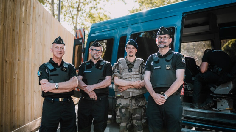 Trois aumôniers de gendarmerie et un aumônier militaire posent devant un irisbus. À gauche un mur de palissade en bois clair