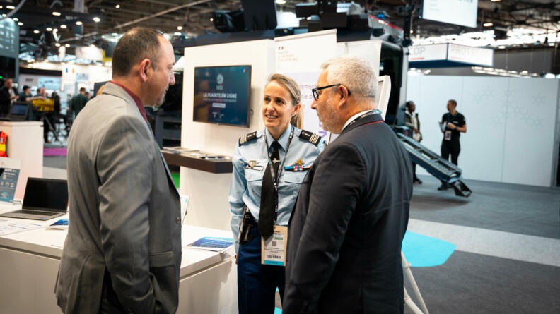 Devant un stand du salon milipol, un femme lieutenant-colonel de gendarmerie &eacute;change avec deux hommes en costume