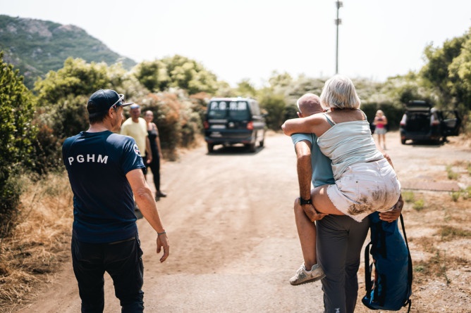 Agrandir l'image Des gendarmes portent secours à une femme blessée. L'un d'eux porte la femme sur son dos. Ils se dirigent en direction du véhicule de la gendarmerie.