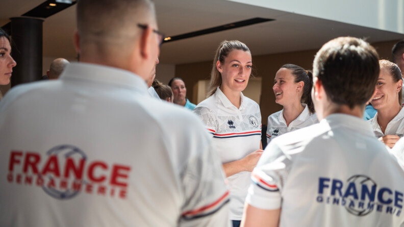 Deux sportifs de la gendarmerie v&ecirc;tus de t-shirts aux couleurs de l'&eacute;quipe de France gendarmerie de volley vus de dos, &eacute;changeant avec trois autres sportives vues de face.