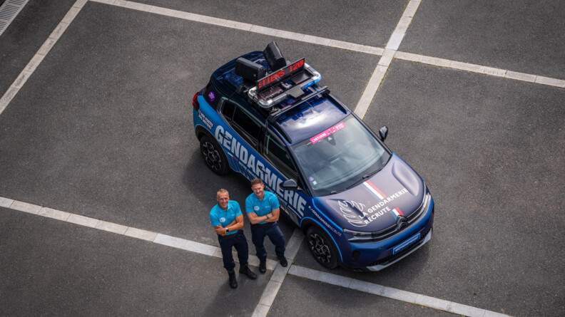 Deux membres de la caravane gendarmerie du Tour de France &agrave; c&ocirc;t&eacute; d'un v&eacute;hicule du Tour de la gendarmerie, vu d'en-haut