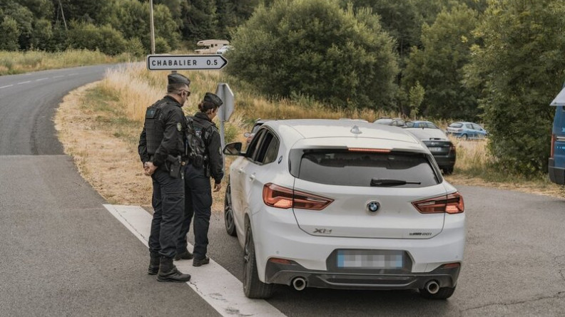 Deux gendarmes, debout, de dos, contr&ocirc;lent un v&eacute;hicule blanc de marque BNW sur une route de campagne