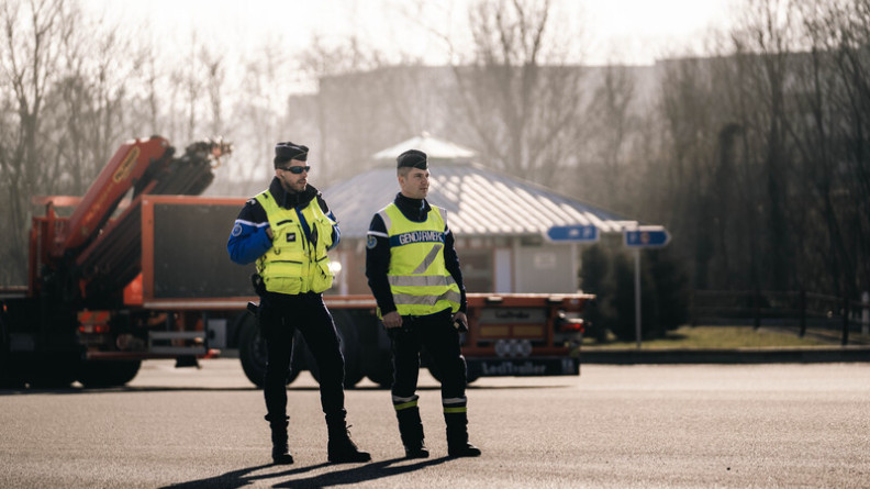 Agrandir l'image Photo de deux gendarmes vêtus d'une chasuble jaune fluo, positionnés au niveau d'une gare de péage de l'autoroute.