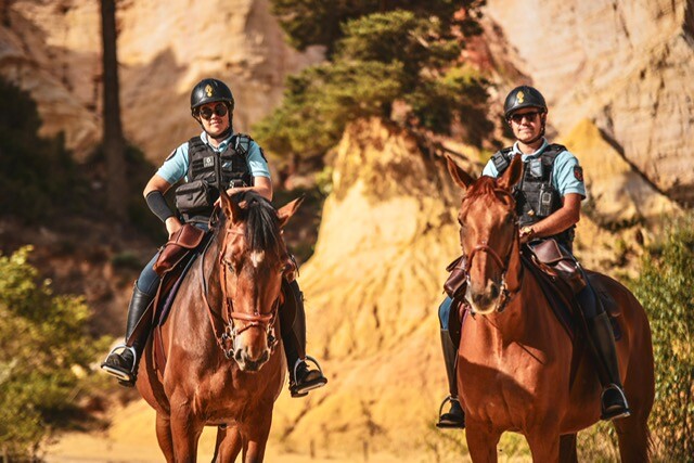 Deux cavaliers gendarmerie sur leur monture, face caméra, dans un paysage minéral de couleur ocre (Rustrel - Vauclause).