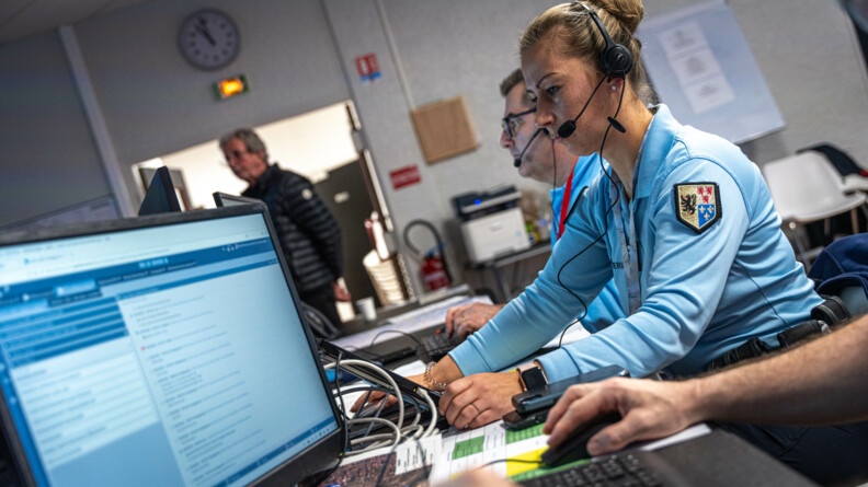 Photo de la commandante Hersand dans le Centre Opérationnel Départemental. Elle est devant des ordinateurs. Elle porte un casque à partir duquel elle peut commmuniquer. Dans le fond, derrière elle on aperçoit un de ses collègues aussi avec un casque et face à un ordinateur.
