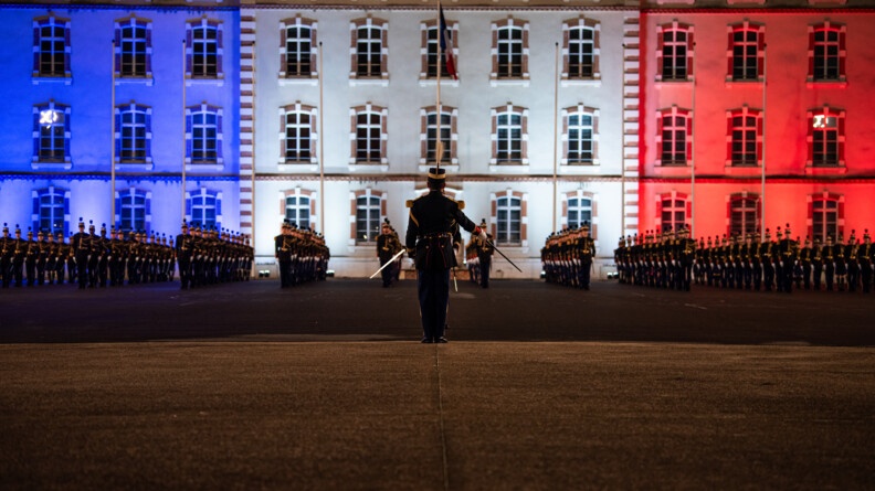 Agrandir l'image Un officier de l'EOGN, de dos, au centre, salue au sabre les deux promotions d'élèves de l'EOGN, alignés devant l'état-major de l'Ecole, illuminé de bleu blanc et rouge