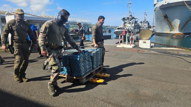 Agrandir l'image Trois militaires du GIGN en treillis font rouler une palette portant des sacs bleus dans des filets noirs sur le quai d'un port