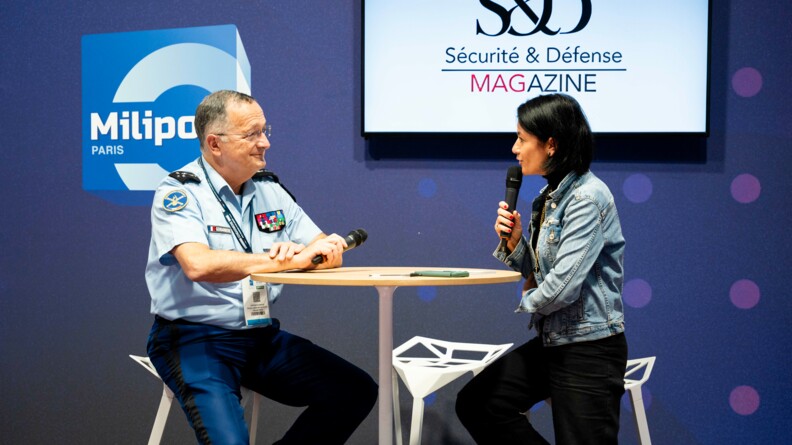 A gauche le directeur g&eacute;n&eacute;ral de la gendarmerie assis sur un tabouret avec un micro, devant un gueridon haut, &eacute;chnageant avec un femme &agrave; droite, assise sur un tabouret, devant un fond bleu sigl&eacute; Milipol et Revue S&eacute;curit&eacute; et d&eacute;fense magazine