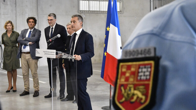 Au premier plan, l'&eacute;cusson d'&eacute;paule d'un gendarme. Au second plan, le ministre de l'Int&eacute;rieur et des Outre-mer faisant une allocution derri&egrave;re un pupitre. Derri&egrave;re lui, les drapeaux fran&ccedil;ais et europ&eacute;en. A ses c&ocirc;t&eacute;s, quatre autorit&eacute;s.