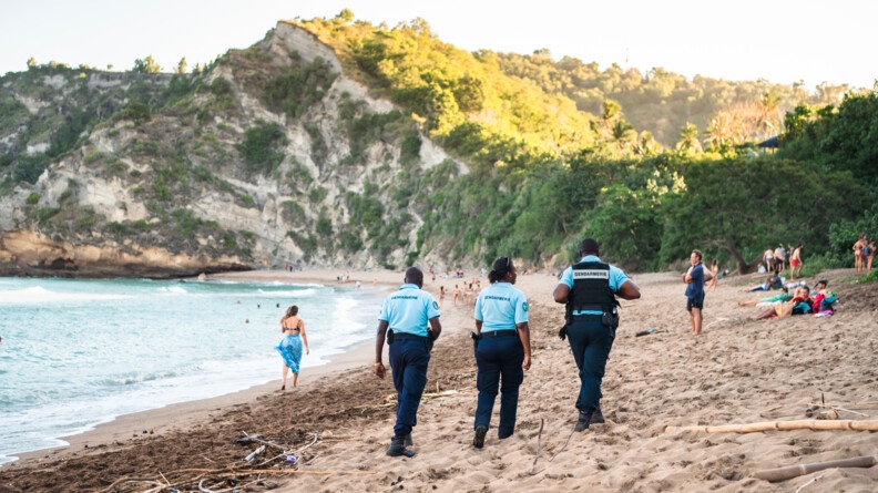 Trois réservistes de dos patrouillent sur une plage où se trouvent des baigneurs.
