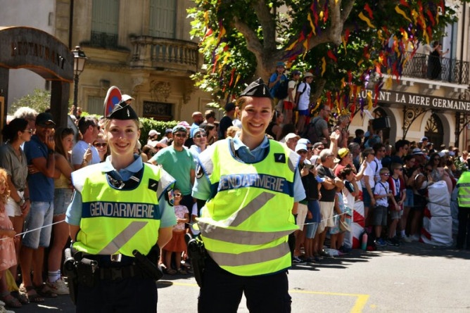 Agrandir l'image Deux jeunes femmes gendarmes, revêtant la chasuble jaune avec l'inscription Gendarmerie, se tiennent debout, côte à côte, dans un village