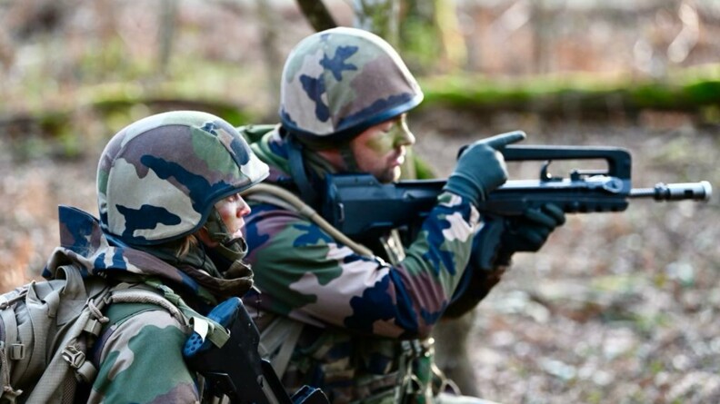 Deux gendarmes de profil, avec de la peinture de cammouflage sur le visage, regardant au loin. L'un d'entre eux pointe une arme.