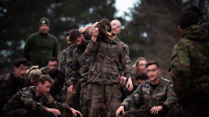 En extérieur, plus de trois militaires portent un tronc de bois. Autour d'eux, d'autres gendarmes sont accroupis