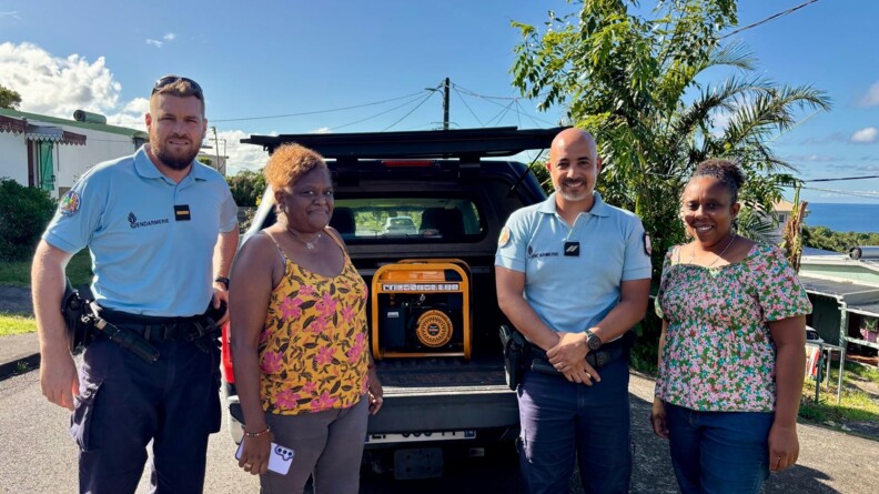 Agrandir l'image Deux gendarmes posent, souriants, autour de deux femmes réunionnaises, qui sourient également, après le passage du cyclone Garance à La Réunion. Le temps ets beau et le ciel est bleu. Les quatre personnes s etrouvent debout dans la rue, devant un véhicule dont le coffre est ouvert, et dévoile un dérouleur de câble.