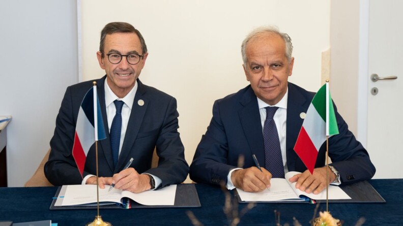 Le ministre de l'Int&eacute;rieur fran&ccedil;ais, &agrave; gauche, et son homologie italien, &agrave; droite, assis &agrave; une table bleue, les drapeaux de la France et de l'Italie pos&eacute;s devant eux. Ils regardent face cam&eacute;ra, alors qu'ils s'appr&ecirc;tent &agrave; signer un document dans un parapheur.