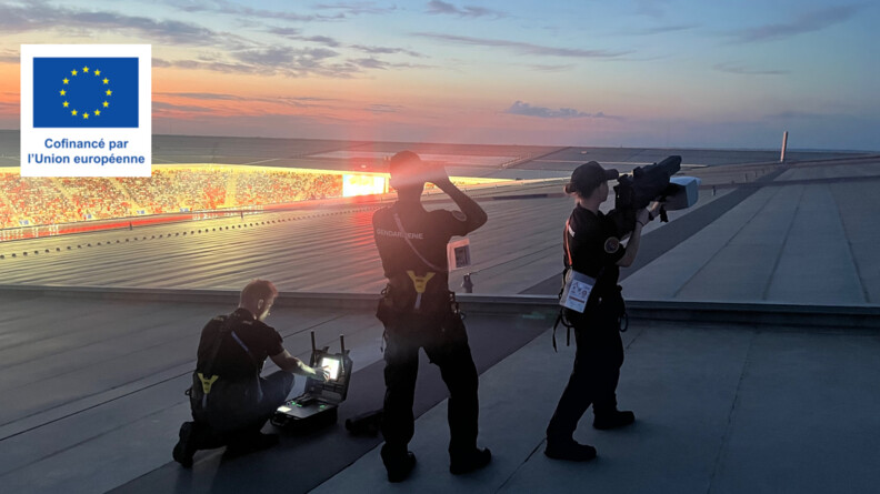 Trois gendarmes vus de dos, sur le toit du stade de Bordeaux : le premier, &agrave; gauche, est agenouill&eacute; devant une mallette contenant un &eacute;cran, le second scrute le ciel avec des jumelles, et la troisi&egrave;me pointe un fusil anti-drone vers le ciel.