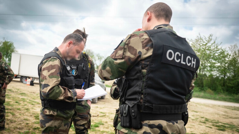 Trois enquêteurs de l'OCLCH gendarmerie en treillis avec chasubles noires en train de prendre des notes sur l'enquête; l'un est de dos à droite, l'autre à gauche est de profil et un autre au second plan, caché par le deuxième.