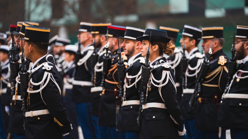 Une gendarme en uniforme se tient debout, de biais, au milieu d'hommes, gendarmes eux-aussi.