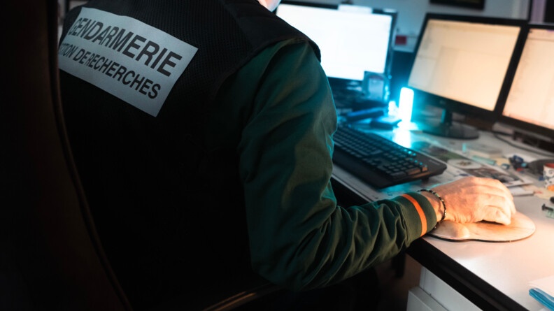 Enquêteur d'une Section de recherches de la gendarmerie de dos devant des écrans d'ordinateur.