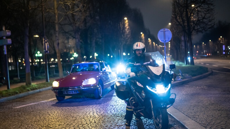 Agrandir l'image Un gendarme en moto de nuit devant des véhicules de collection