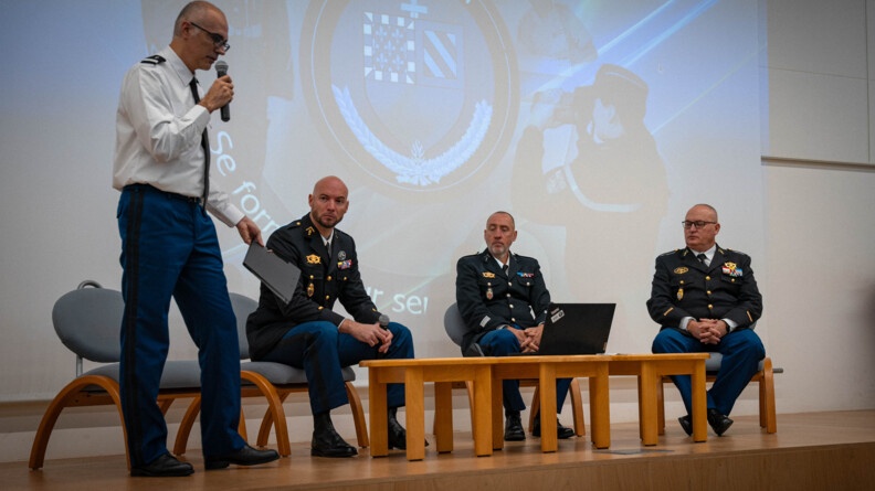 Quatre militaires se tiennent sur une estrade. L'un d'eux est debout, portant un micro &agrave; sa bouche. Les trois autres sont assis c&ocirc;te &agrave; c&ocirc;te, &eacute;coutant le gendarme se trouvant debout. Derri&egrave;re eux,  un grand &eacute;cran projette un &eacute;cusson sur lequel est inscrit "Ecole de Dijon"