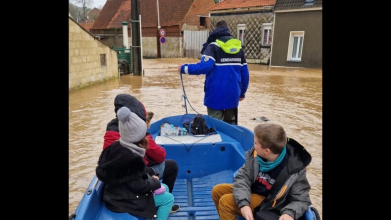 un gendarme tire une barque dans une zone inond&eacute;e. Dans l'embarcation, se trouve deux enfants, un adulte et un petit chien.