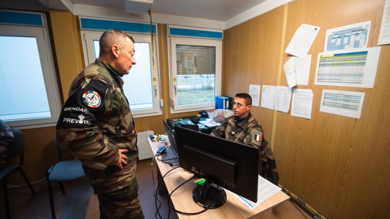 Agrandir l'image A gauche, de profil droit, les mains sur les hanches, un prévôt échange avec un lieutenant de l'armée, assis derrière son ordinateur