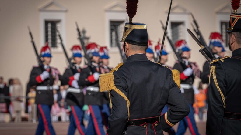 Deux militaires de la garde républicaine de dos, en arrière plan en flou les gardes de monaco défilent